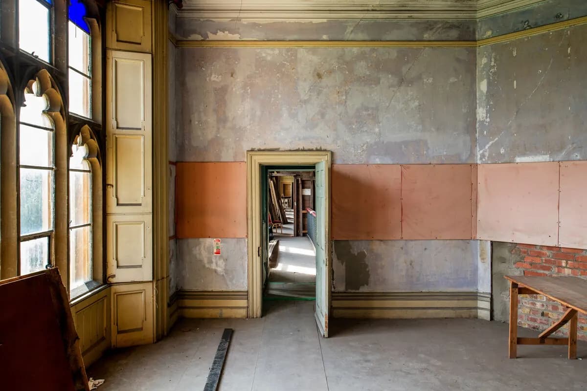An unused room at Ashton Court Mansion with peeling walls and tall Gothic windows
