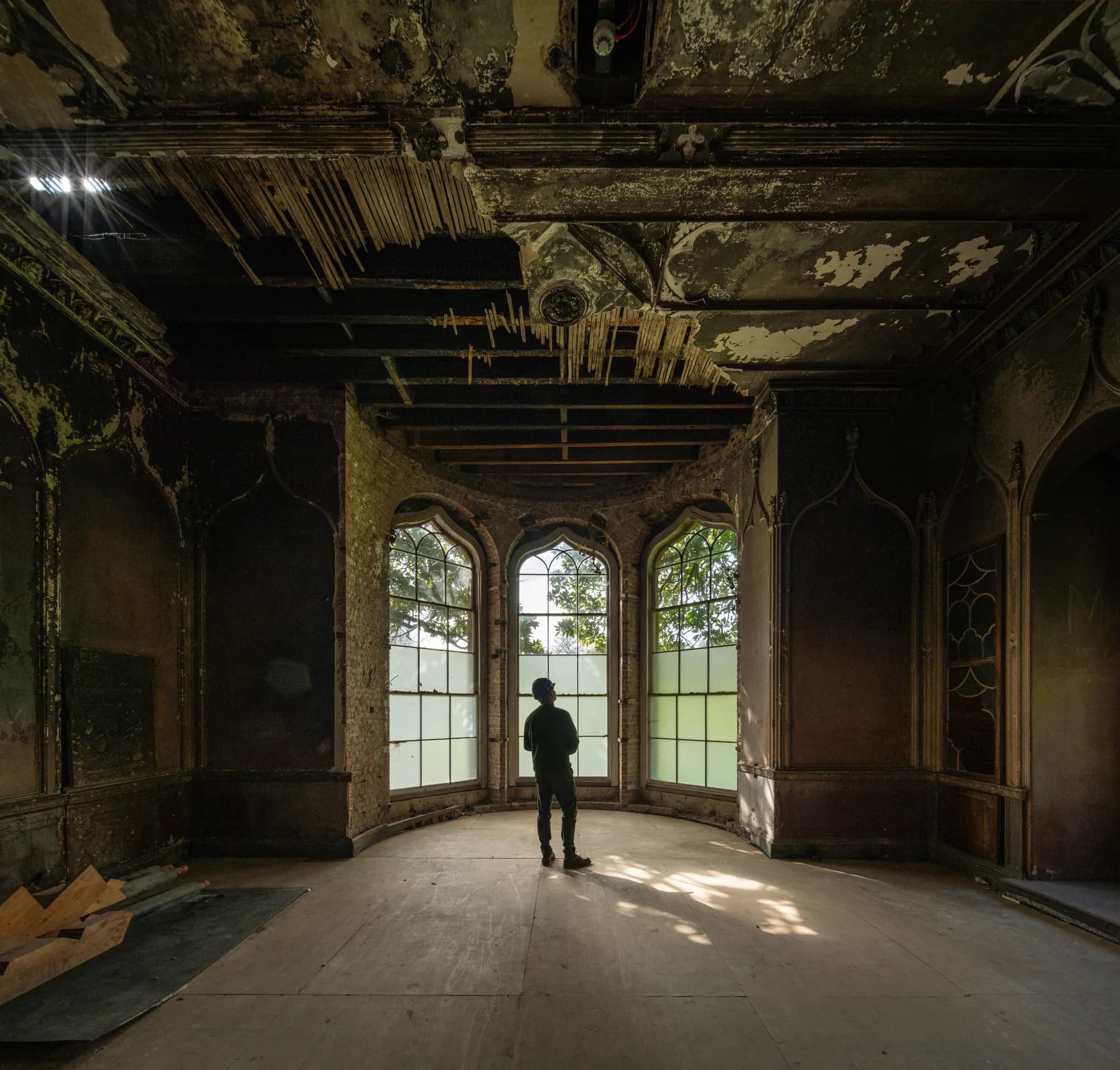 A visitor looking out of the Gothic bay windows of an unrestored room at Ashton Court Mansion