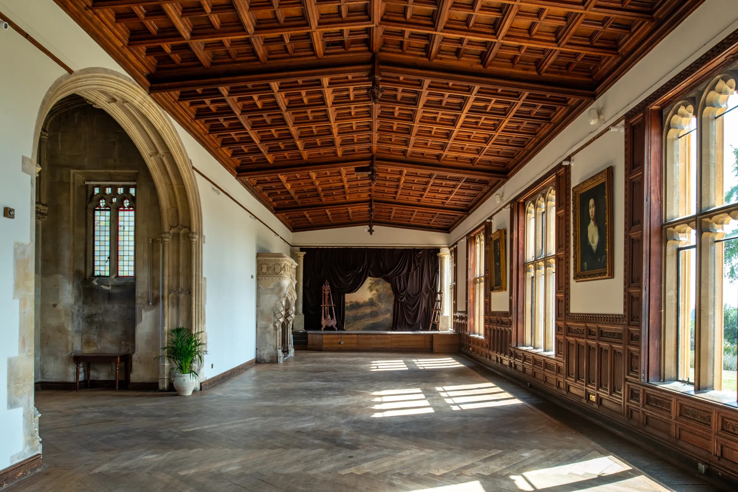 A sunlit room at Ashton Court Mansion with a coffered timber ceiling, panelled walls and a parquet floor